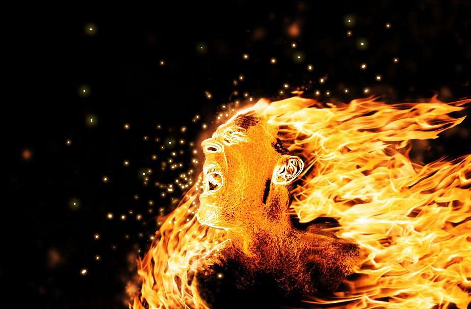 A face emerging from sweeping orange flames and sparks.